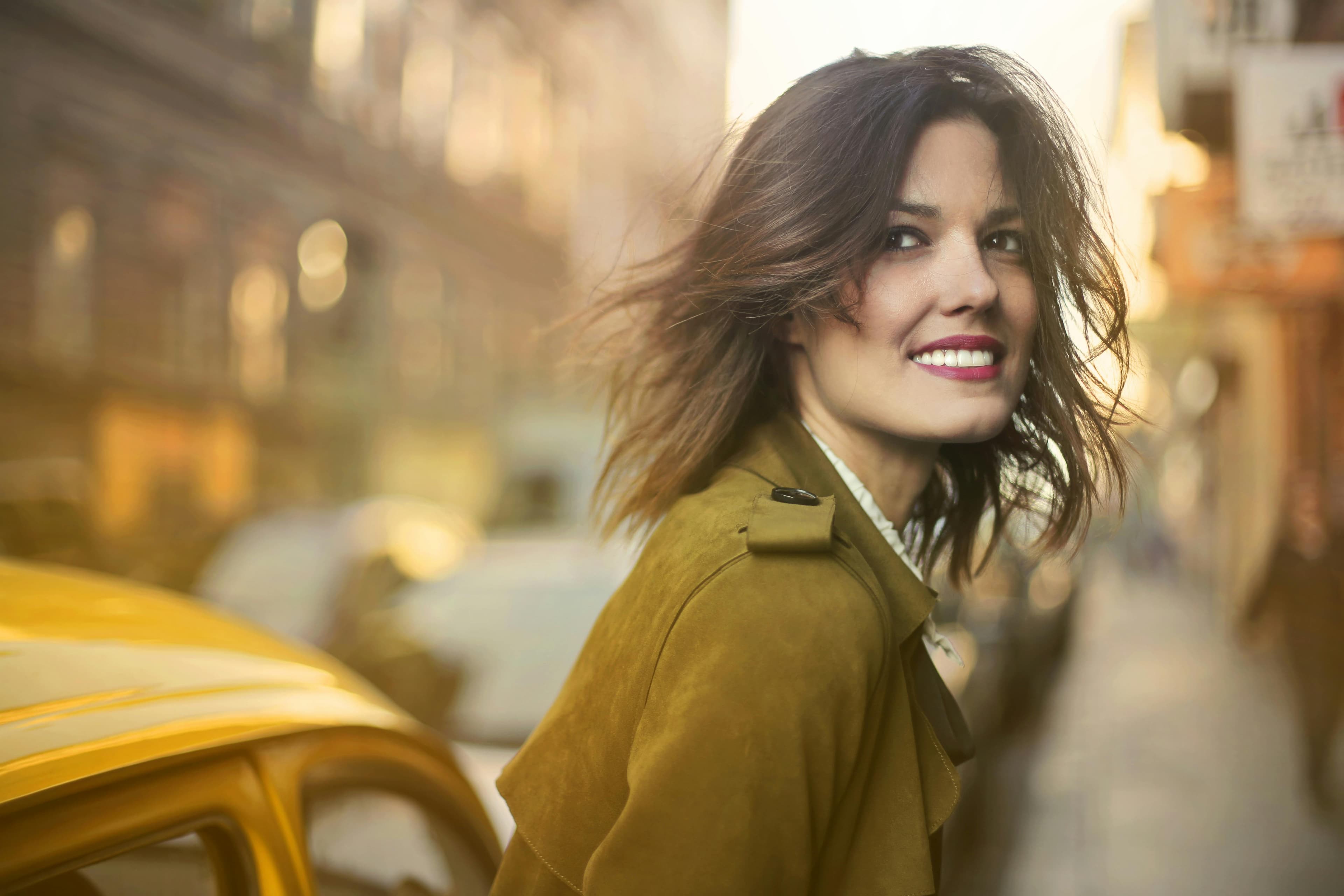 A woman in a mustard suede coat glances back over her shoulder on a city street