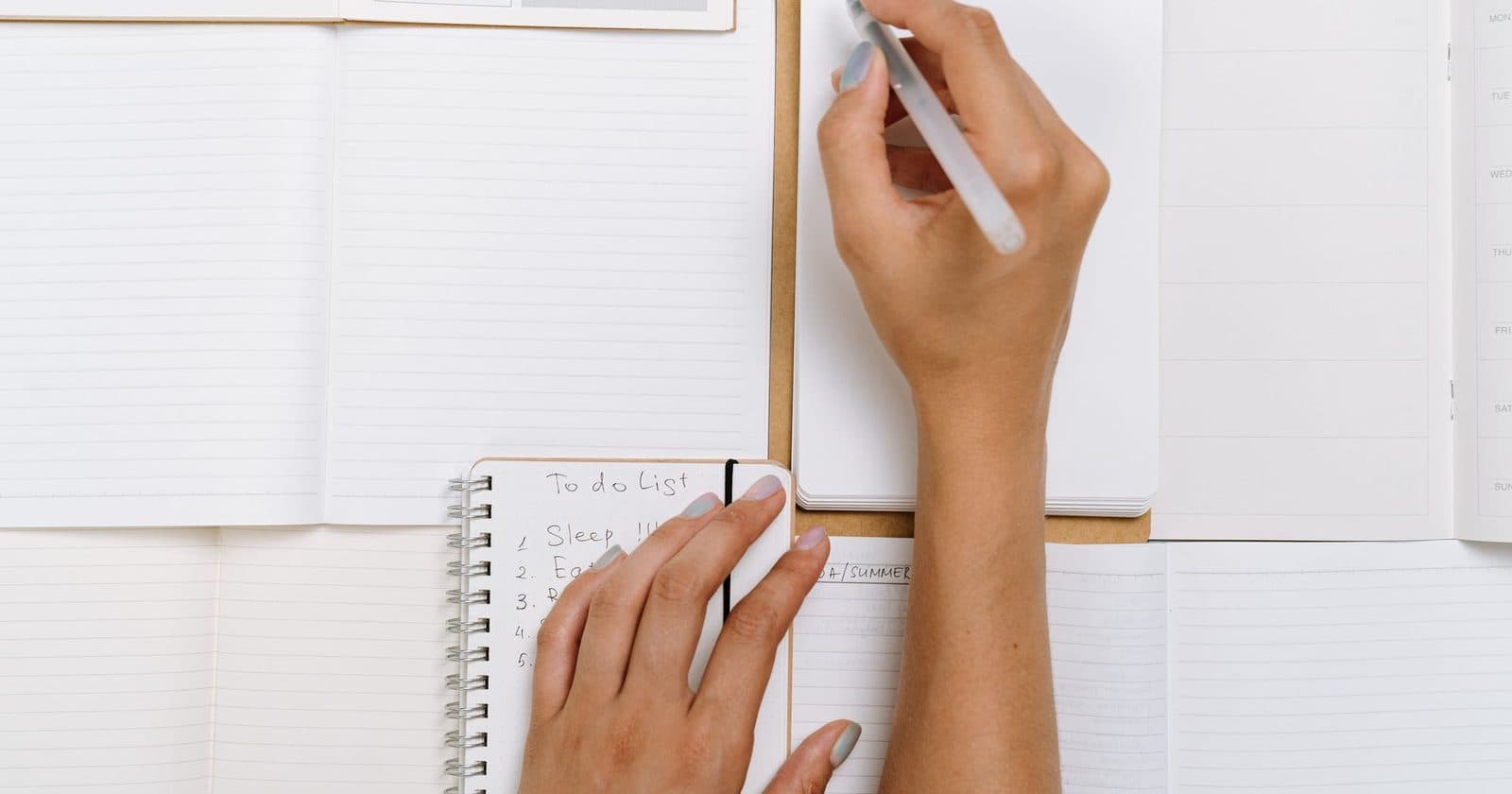 Seen from above, one hand writes in a notebook while the other rests on a small to do list that starts with sleep and eat