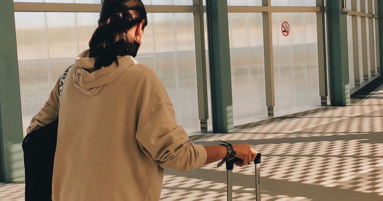 A woman with a suitcase walks through a sunlit airport corridor